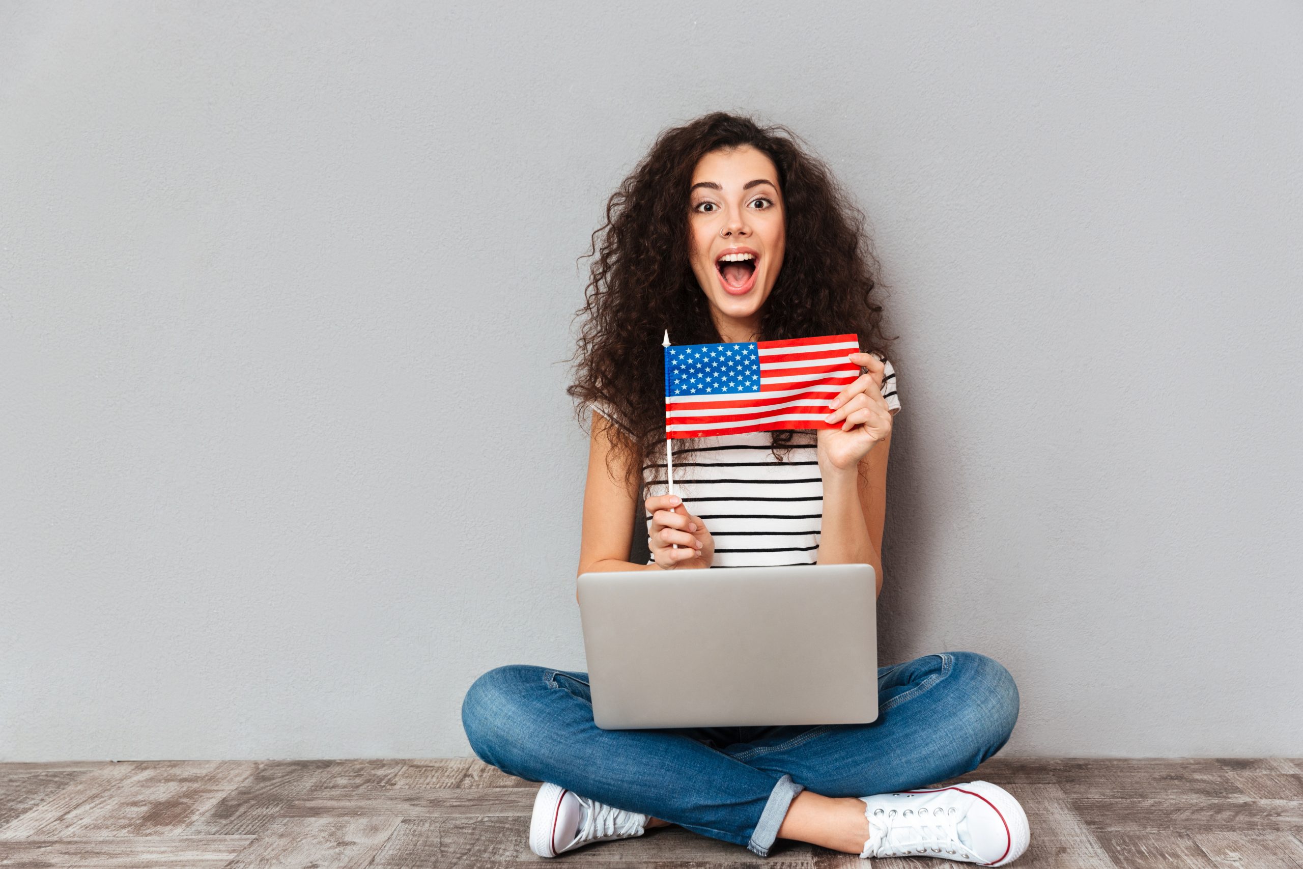gorgeous female with beautiful smile sitting lotus pose with silver computer legs demonstrating american flag grey wall